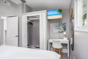 A bedroom with a bed, a desk, and a TV on the wall.