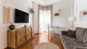 Un soggiorno con un mobiletto in legno, un televisore a schermo piatto, un divano grigio, un tavolo da pranzo con sedie e un'ampia finestra con tende.