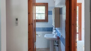 Ein schmaler Flur, der zu einem Badezimmer mit Waschbecken, Fenster und einer weißen Wandklimaanlage führt.
