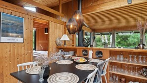 A wooden interior with a dining table set with placemats, chairs, and a vase of dried flowers.