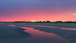 Une plage au coucher du soleil, avec une mer calme qui reflète le ciel.