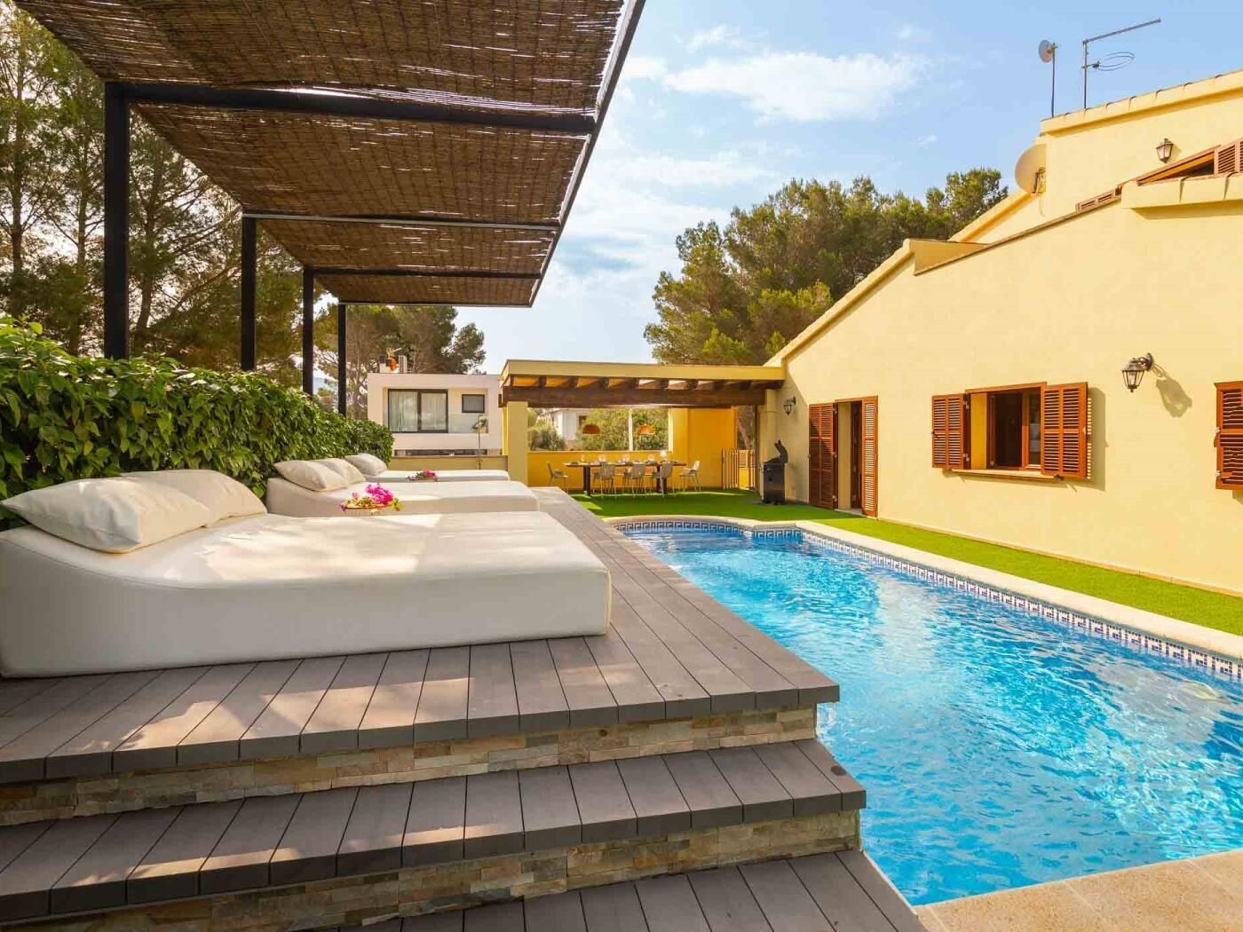 A poolside area with a wooden deck, a white outdoor sofa, and a covered seating area.