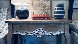 Une console en bois ornée d’un panneau décoratif, une lampe, un livre intitulé « L’investisseur intelligent » et un vase à rayures.
