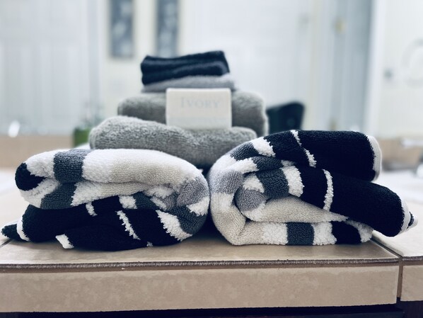 A stack of folded towels in various colors and patterns, with a sign that reads "Ivory" on top. - Chic brick interior condo lit by string lights (Midland)
