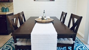 Une table à manger recouverte d’une nappe blanche, entourée de chaises en bois, posée sur un tapis à motifs.