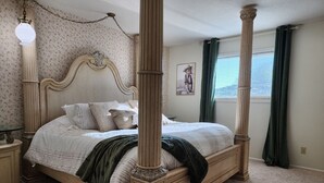 Una cama con dosel con un fondo de papel tapiz floral, un cuadro en la pared y una ventana con cortinas.