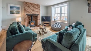 Una sala de estar con chimenea de ladrillo, sofás verdes, un televisor y un ventanal grande.
