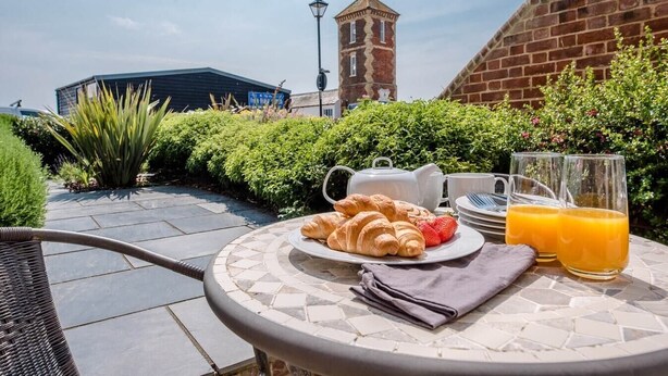 A breakfast setup with croissants, a strawberry, and orange juice on a patio with a brick wall and greenery in the background. - Trehafod, Aldeburgh (Aldeburgh)