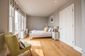 Une chambre à coucher avec un lit, des tables de chevet, une chaise, un radiateur et une fenêtre avec des rideaux.
