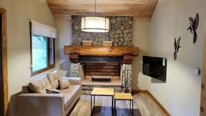 Ein gemütliches Wohnzimmer mit Kamin aus Stein, Holzboden und einem modernen Fernseher an der Wand.