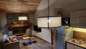 Ein gemütliches Wohnzimmer mit Kamin aus Stein, Holzboden und einer modernen Küche mit Edelstahl-Kühlschrank.