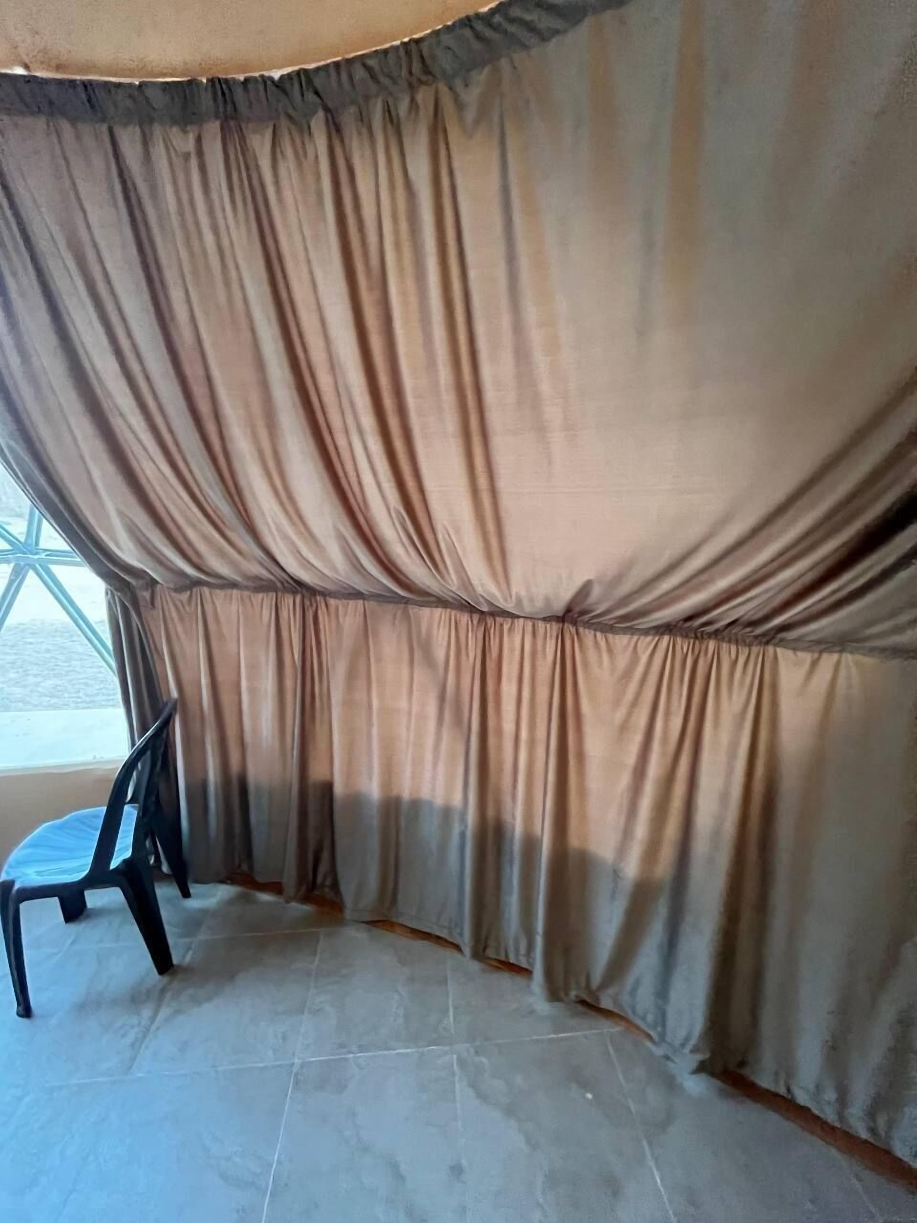 Quarto com uma janela grande, uma cadeira e cortina.