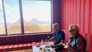Habitación con un ventanal grande que ofrece vistas a un paisaje desértico. Se aprecia una mesa con comida y botellas de agua.
