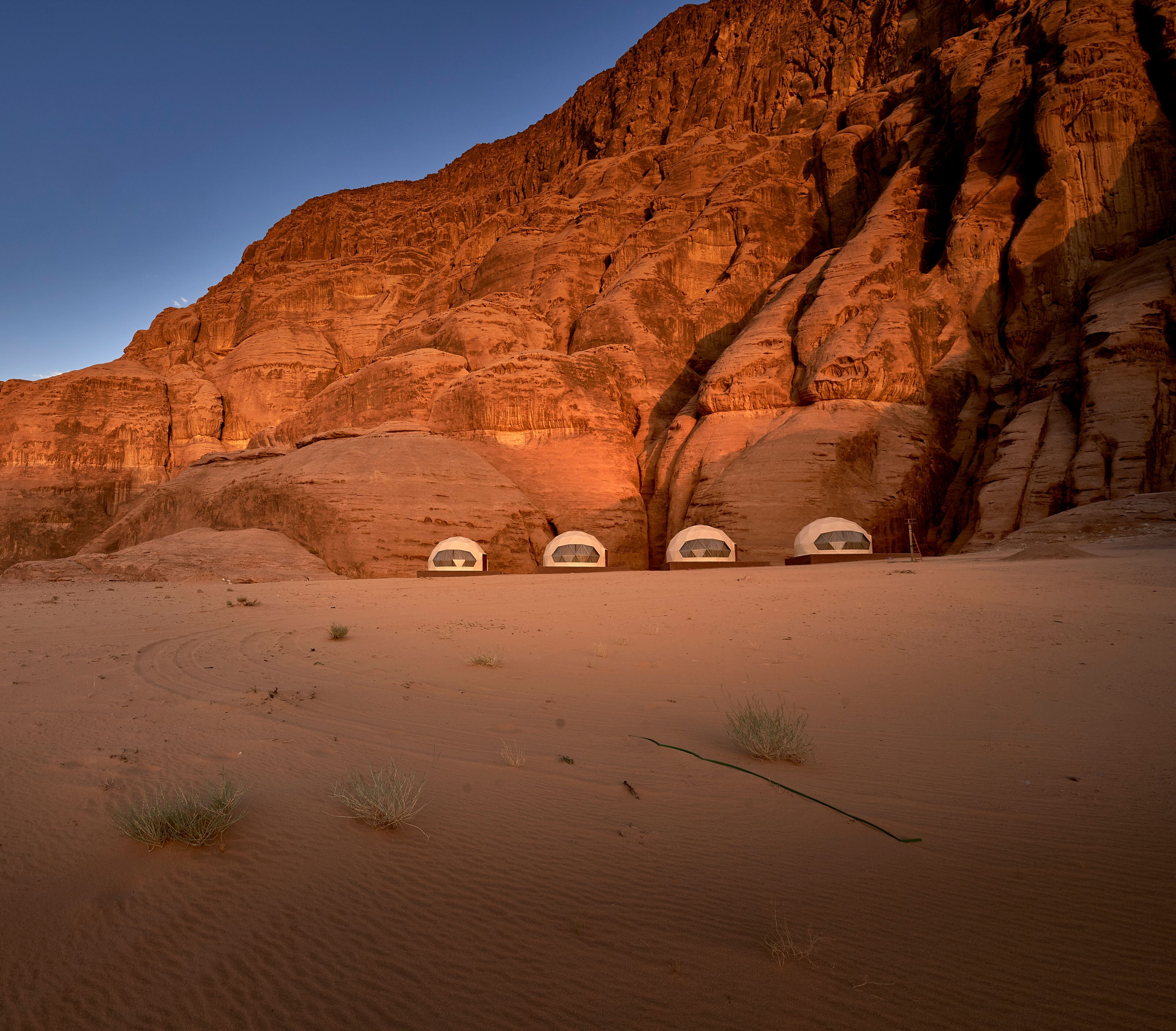 A desert landscape with four white tents against a rocky cliff.