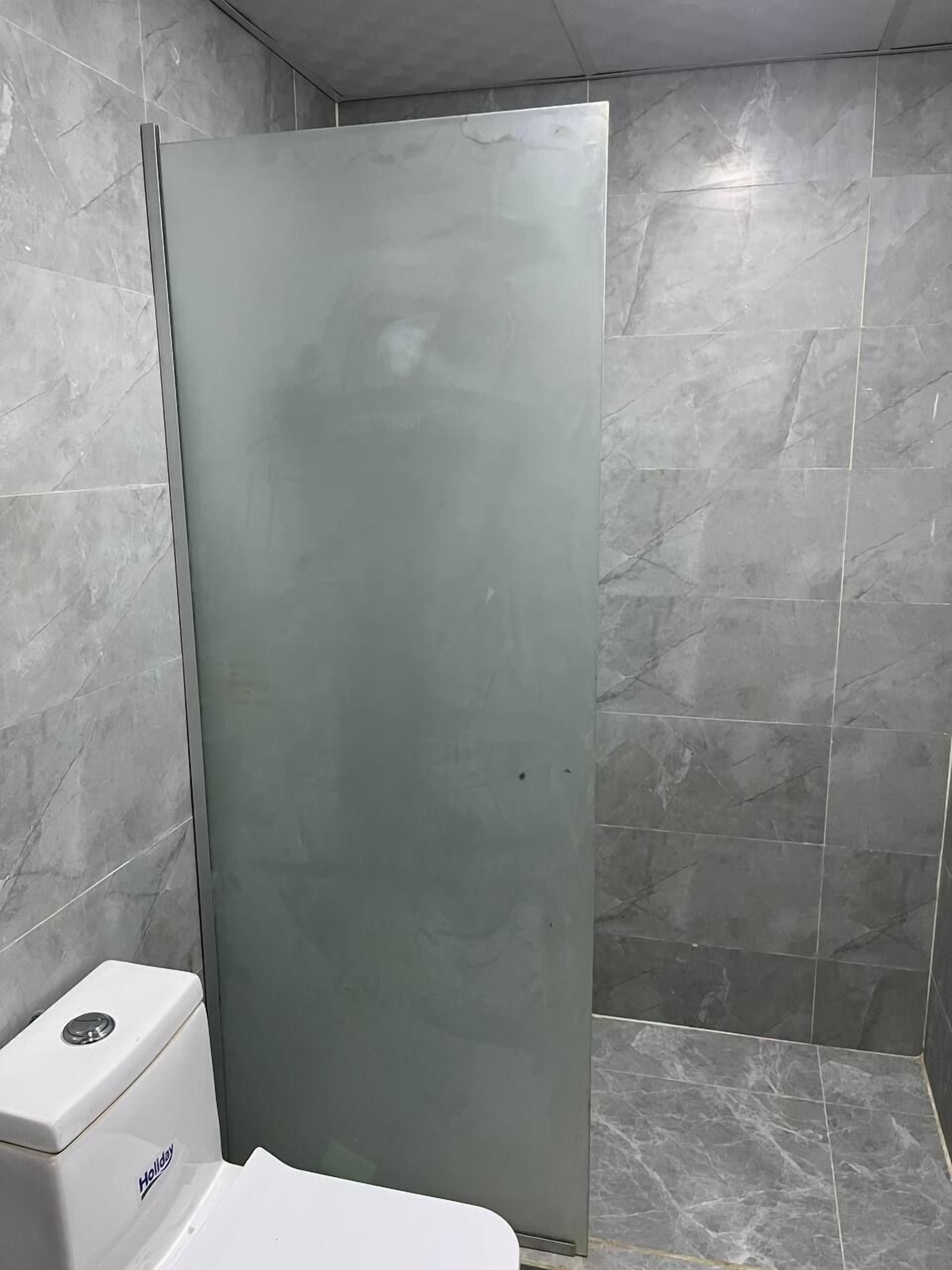 Un baño con inodoro, cabina de ducha y azulejos de mármol gris.