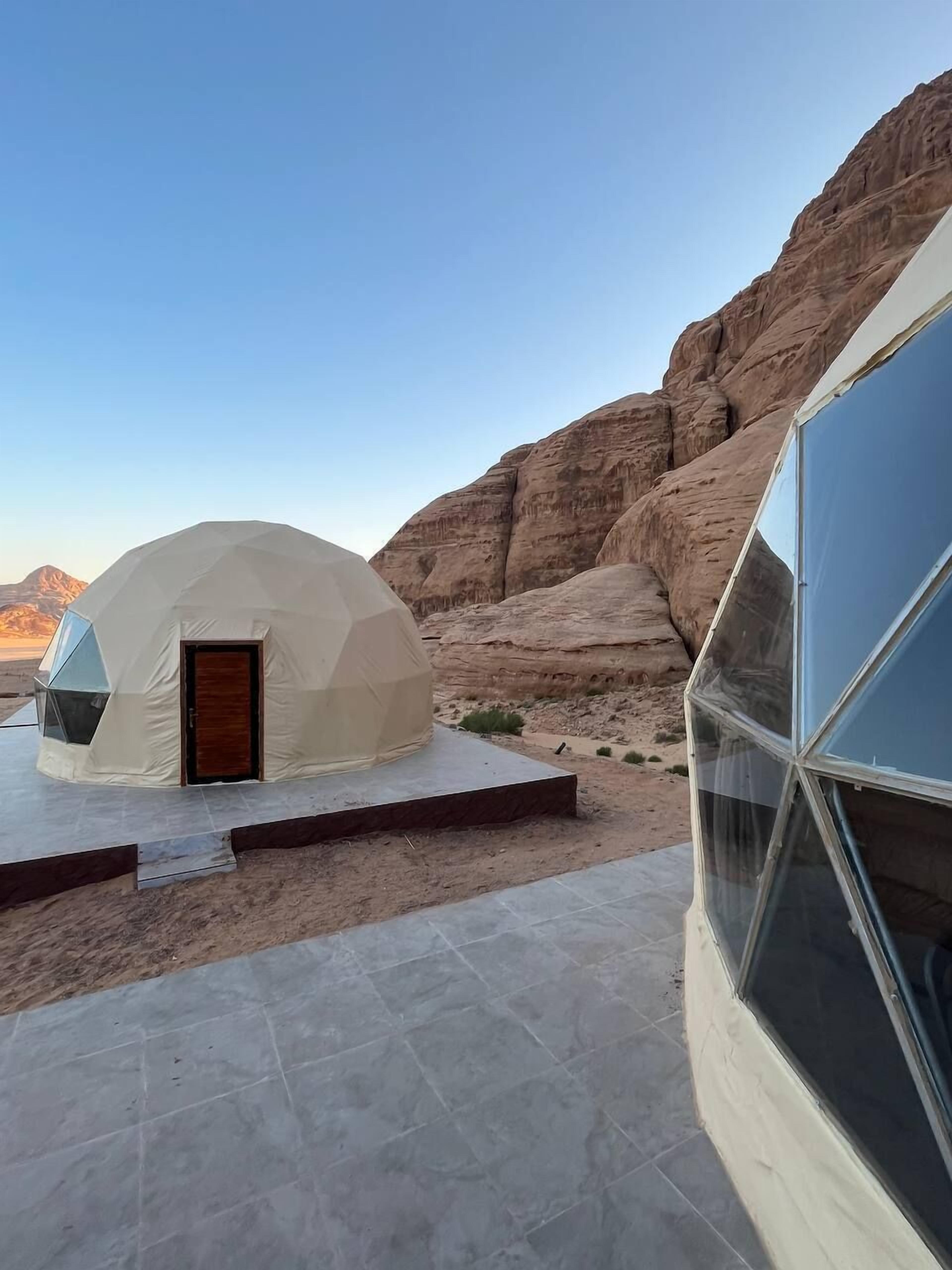 A geodesic dome structure with a wooden door, set against a desert backdrop with rocky formations.