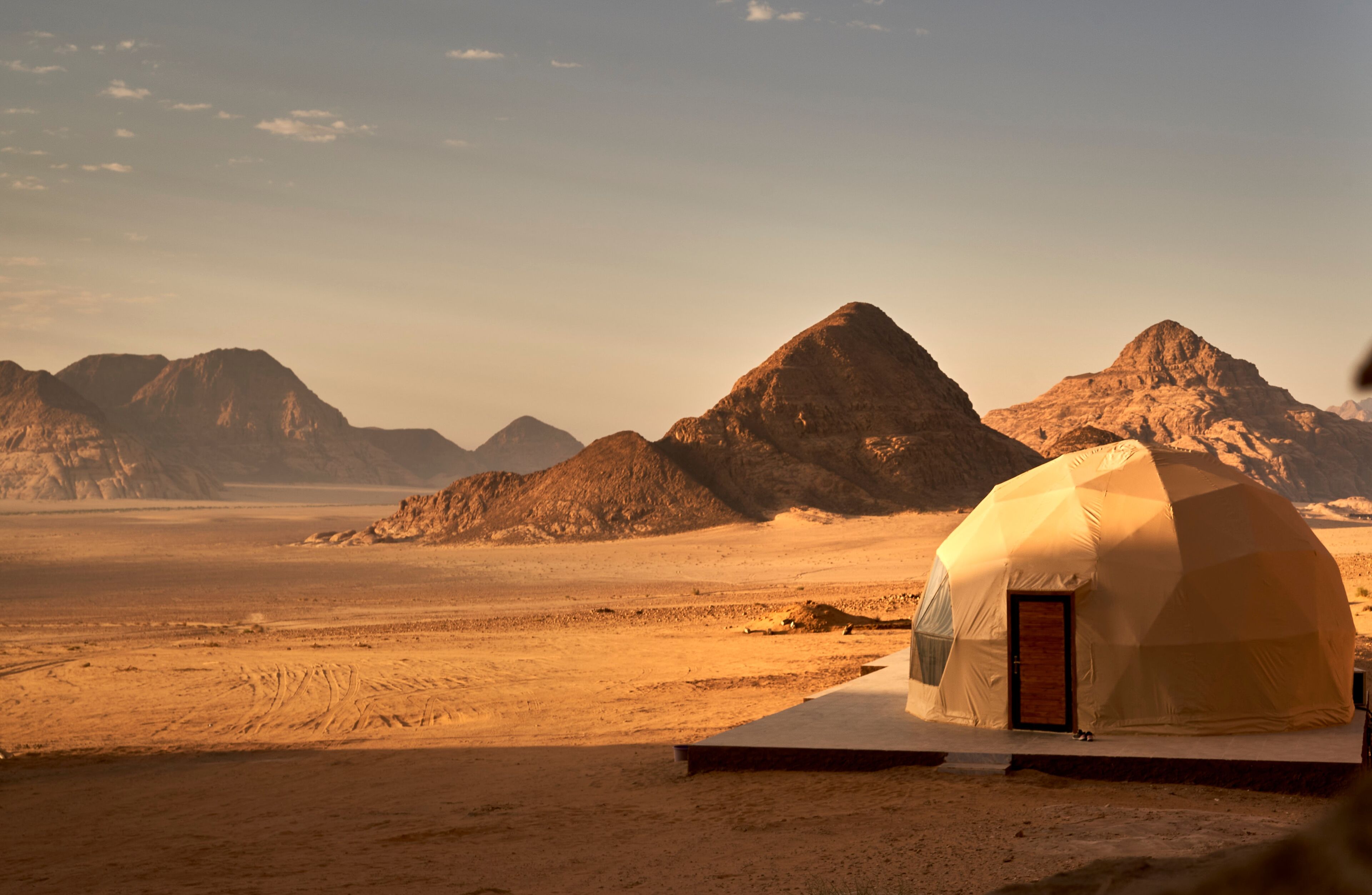 A desert landscape with a large, dome-shaped tent-like structure in the foreground.
