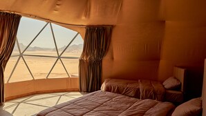 Un dormitorio amplio con una cama grande, varios almohadones y vistas a un paisaje desértico a través de una ventana.
