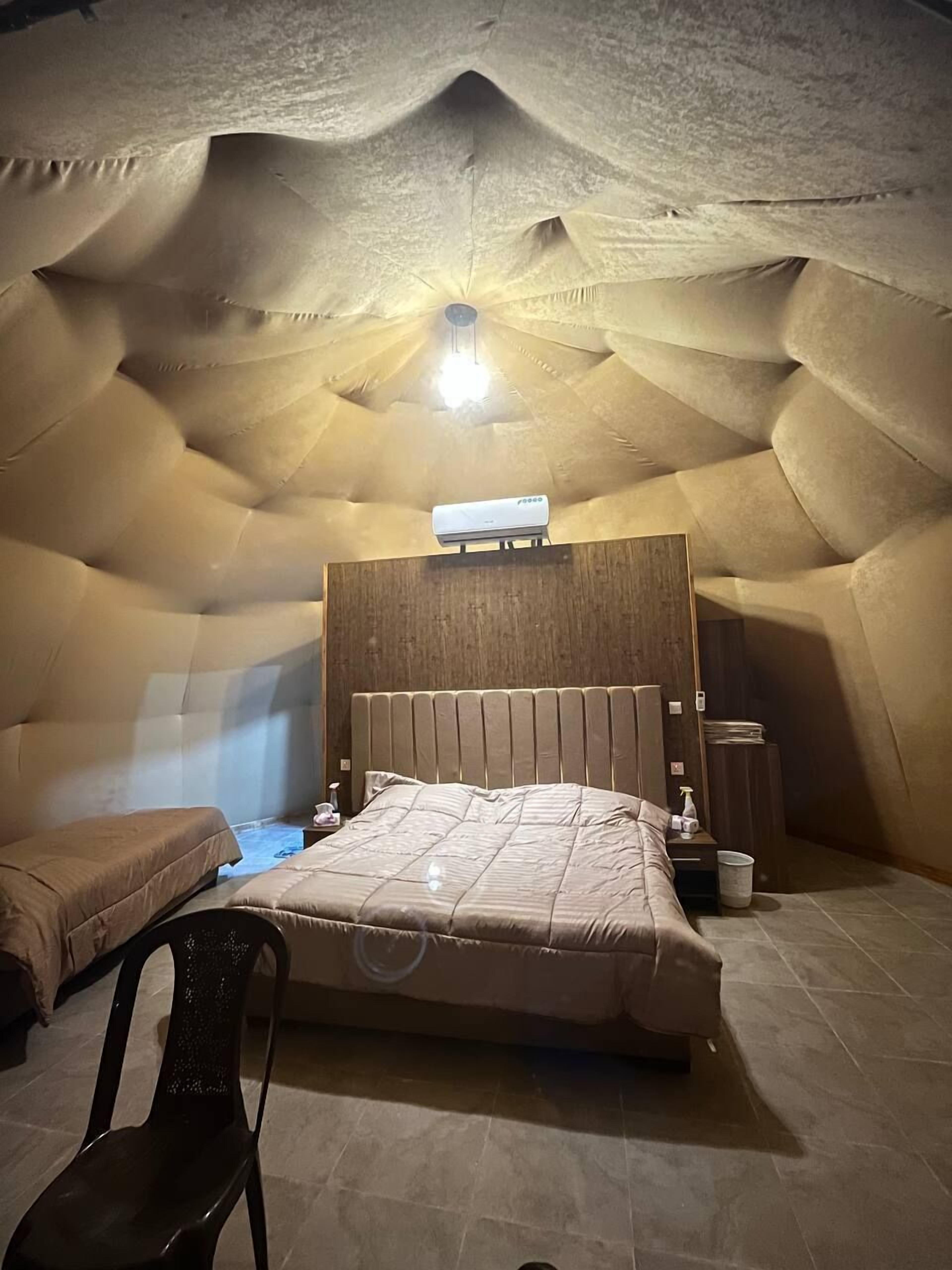 An arched room with a bed, a chair, and a ceiling light.