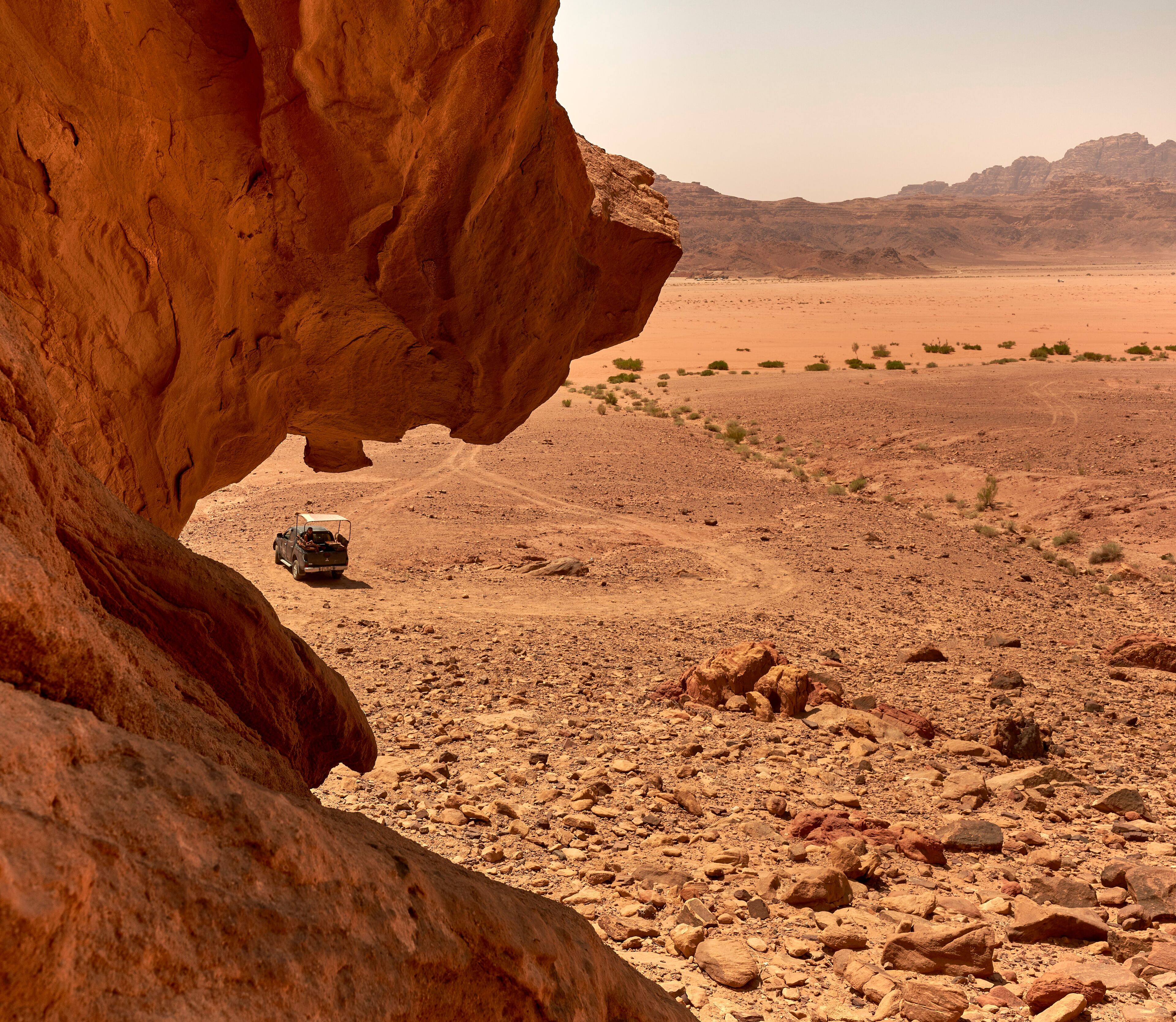 A desert landscape with a rocky overhang and a vehicle on a dirt road.