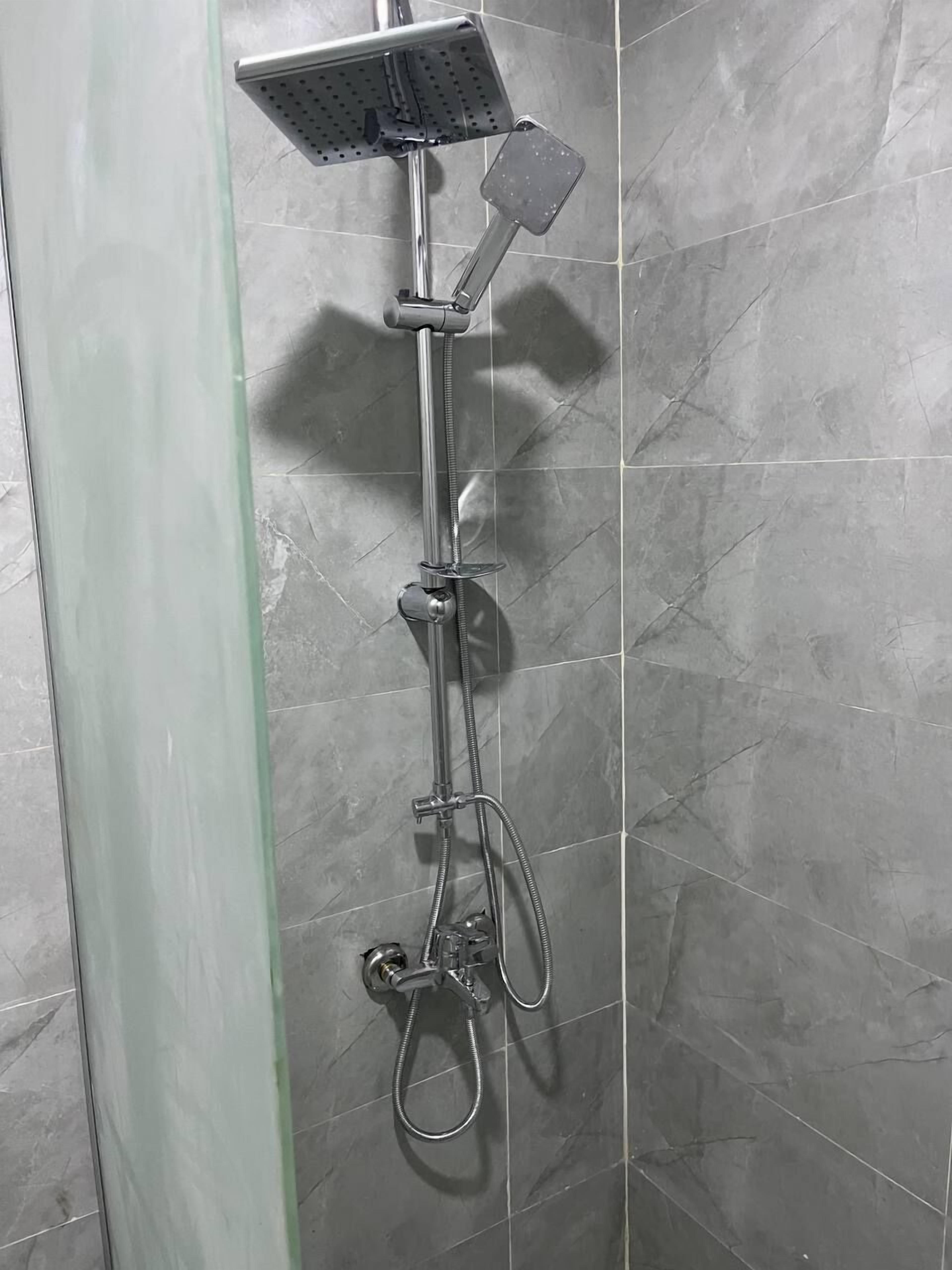A shower with a handheld showerhead and a handheld scrubber mounted on the wall.