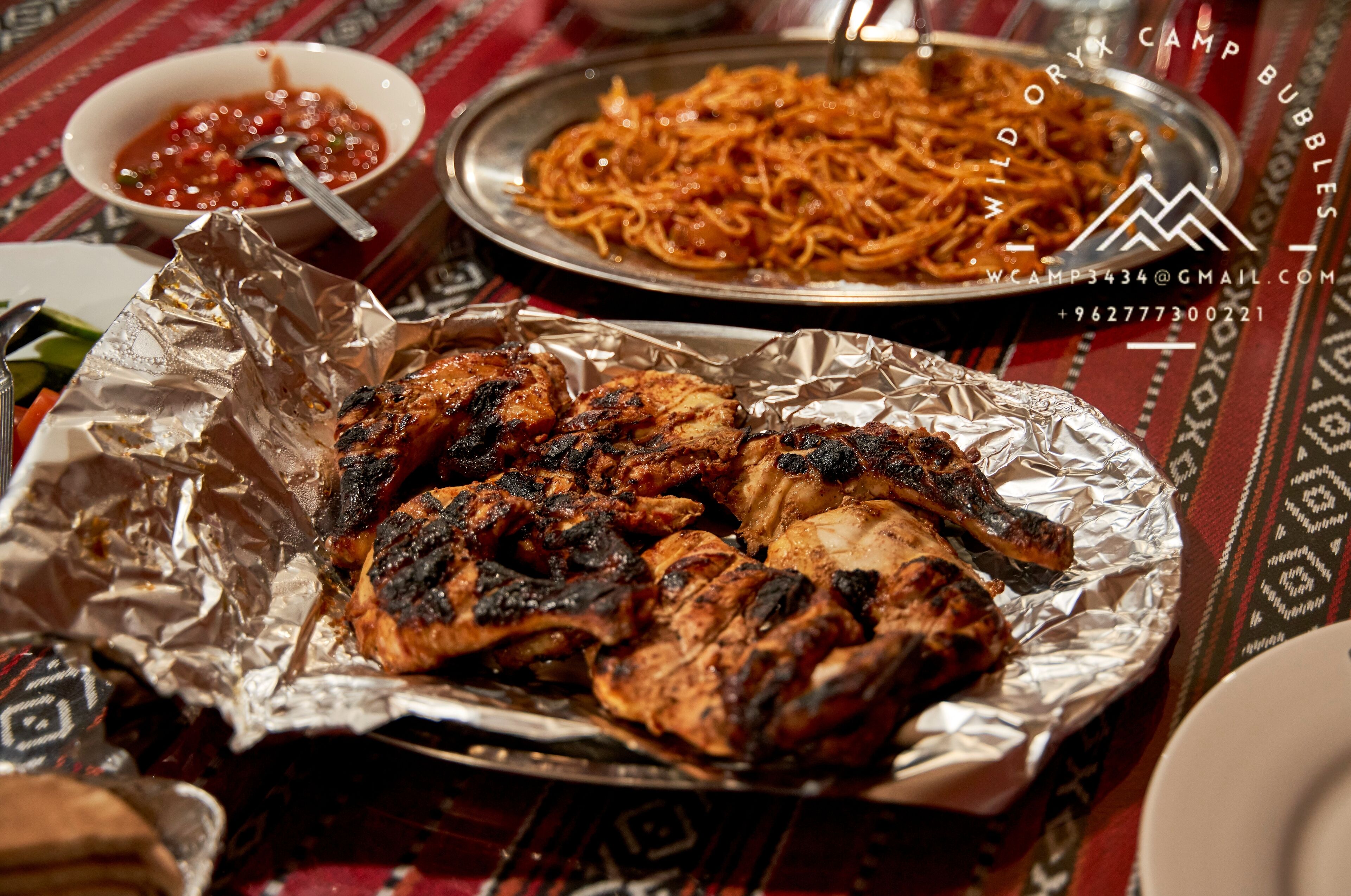 Una mesa con una variedad de platos, incluyendo carne a la parrilla, fideos y un tazón de salsa.