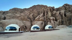Tres estructuras en forma de cúpula con un diseño de ventanas geométricas, sobre un paisaje desértico rocoso.
