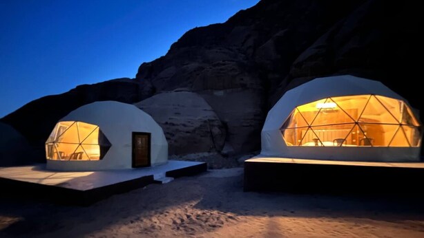 Dos estructuras en forma de geodésica con iluminación cálida, situadas frente a un escarpado acantilado.