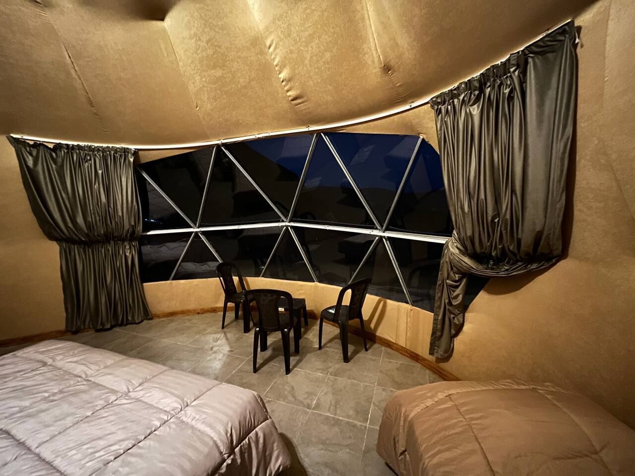 Ein Zimmer mit einer außergewöhnlichen, gewölbten Decke, zwei Betten, einem kleinen Tisch mit Stühlen und einem großen Fenster mit Vorhängen.