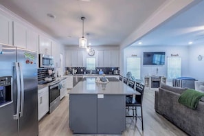A modern kitchen with stainless steel appliances, a central island, and a dining area with a grey sofa. - 10 Beds sleeps 16 with Arcade GAME ROOM & POOL! (Orange Beach)