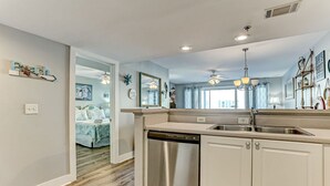 A modern kitchen with white cabinetry, a stainless steel dishwasher, and a large window. - "Spritz By The Sea” is your beach side paradise! (Tybee Island)