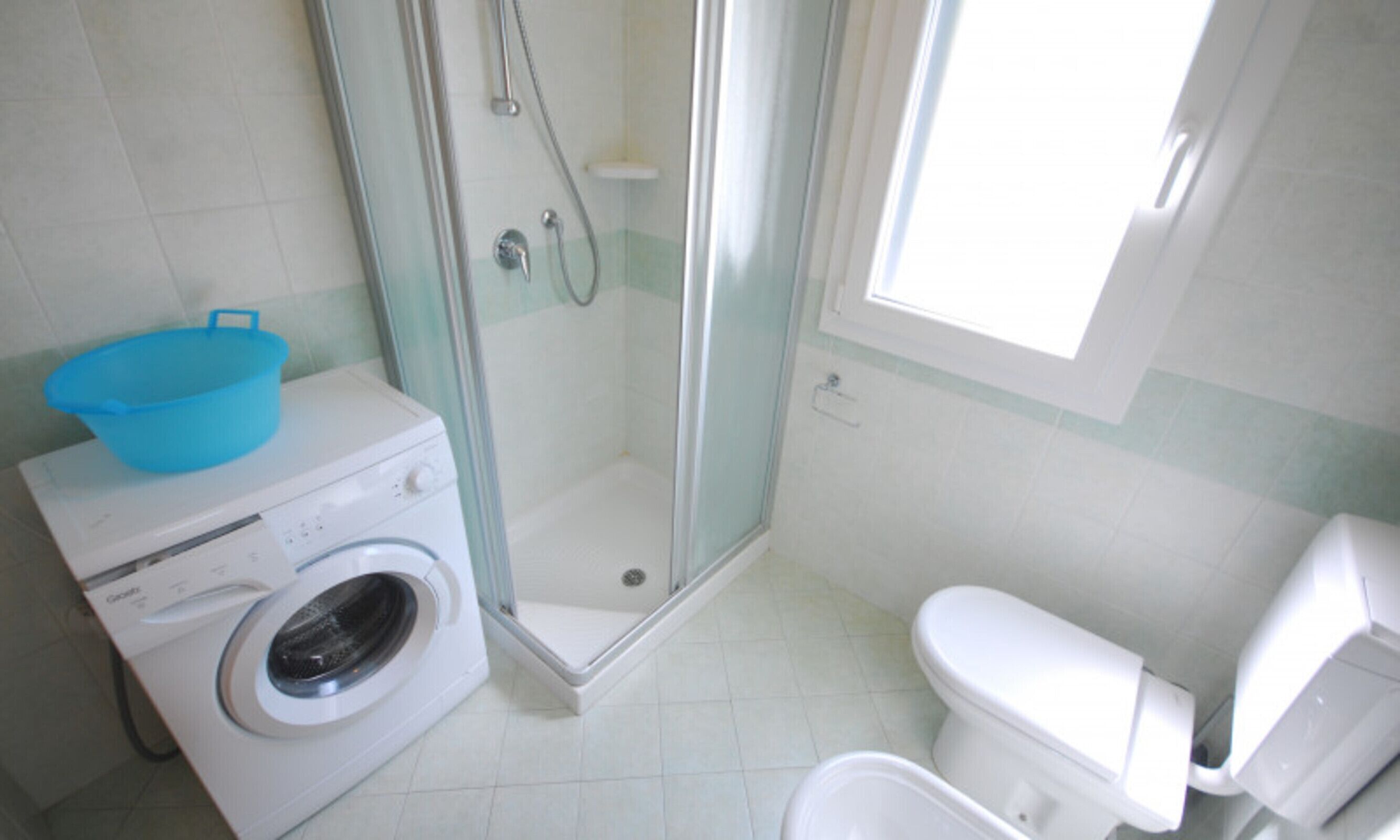 Casa de banho compacta com máquina de lavar, cabine de chuveiro em vidro e sanita.