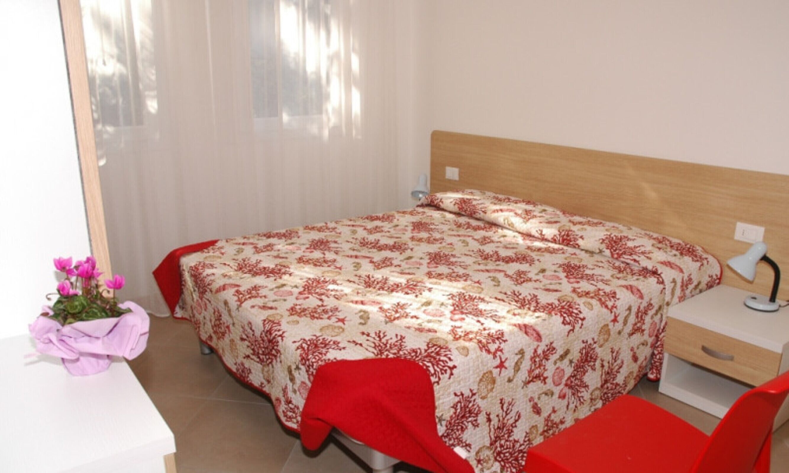 Un dormitorio con cama, mesita de noche, lámpara y una silla.