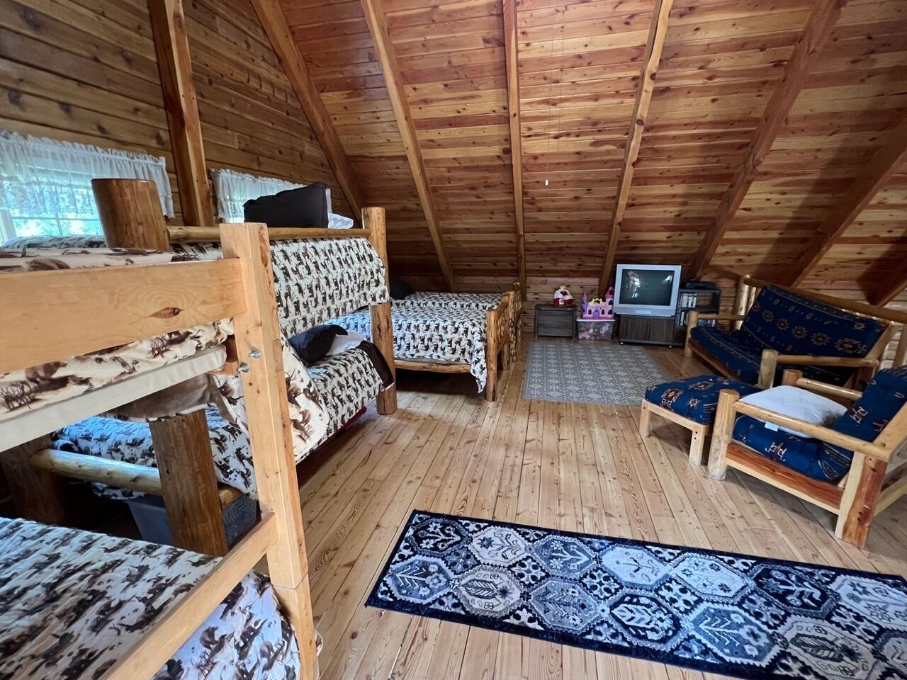A cozy attic room with wooden floors, a patterned rug, bunk beds, a sofa, and a television.