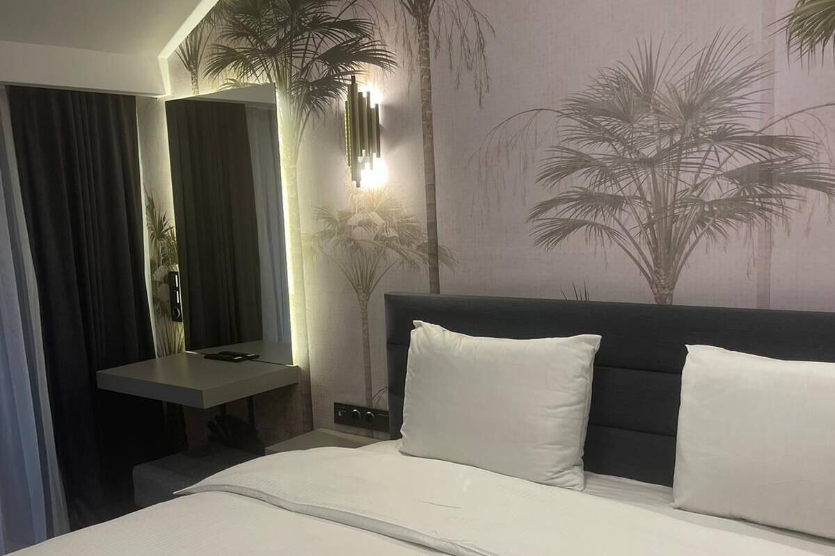Habitación de hotel con una cama grande, una mesita de noche, un espejo y un mural en la pared con palmeras.