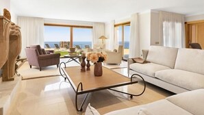 A spacious living room with a large window offering a view of the sea, a sofa, a coffee table, and a fireplace. - Villa Luna Suites (Puigderrós)