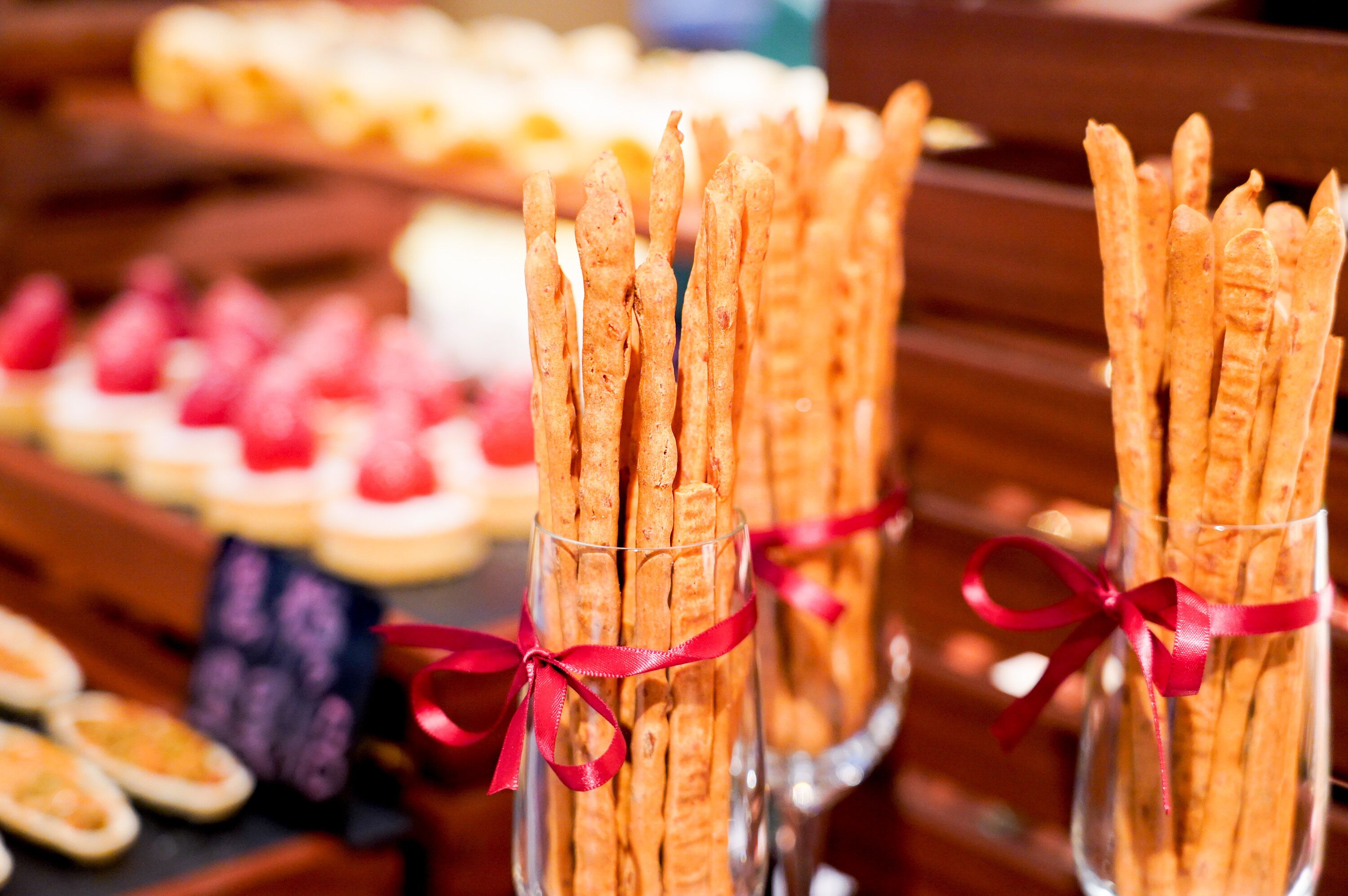 A display of assorted pastries and breadsticks in clear glass containers, tied with red ribbons.