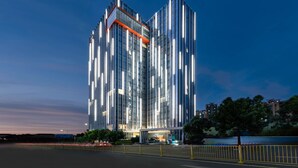 Ein modernes Hochhaus mit reflektierenden Glasfassaden und einem markanten orangefarbenen Akzent im oberen Bereich.