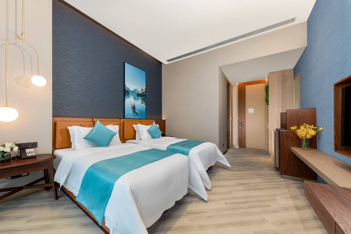 A hotel room with two beds, a desk, a TV, and a painting on the wall.