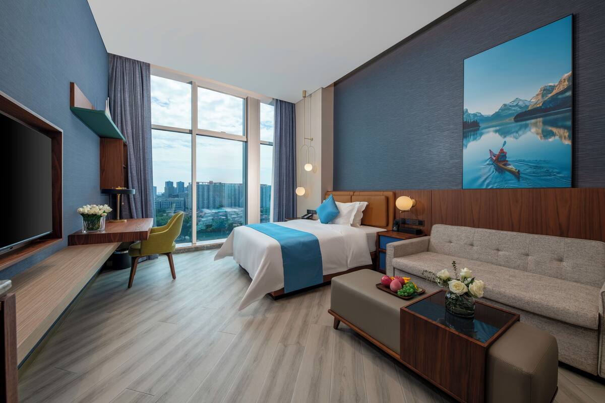 A modern hotel room with a large bed, a sofa, a desk, and a television.