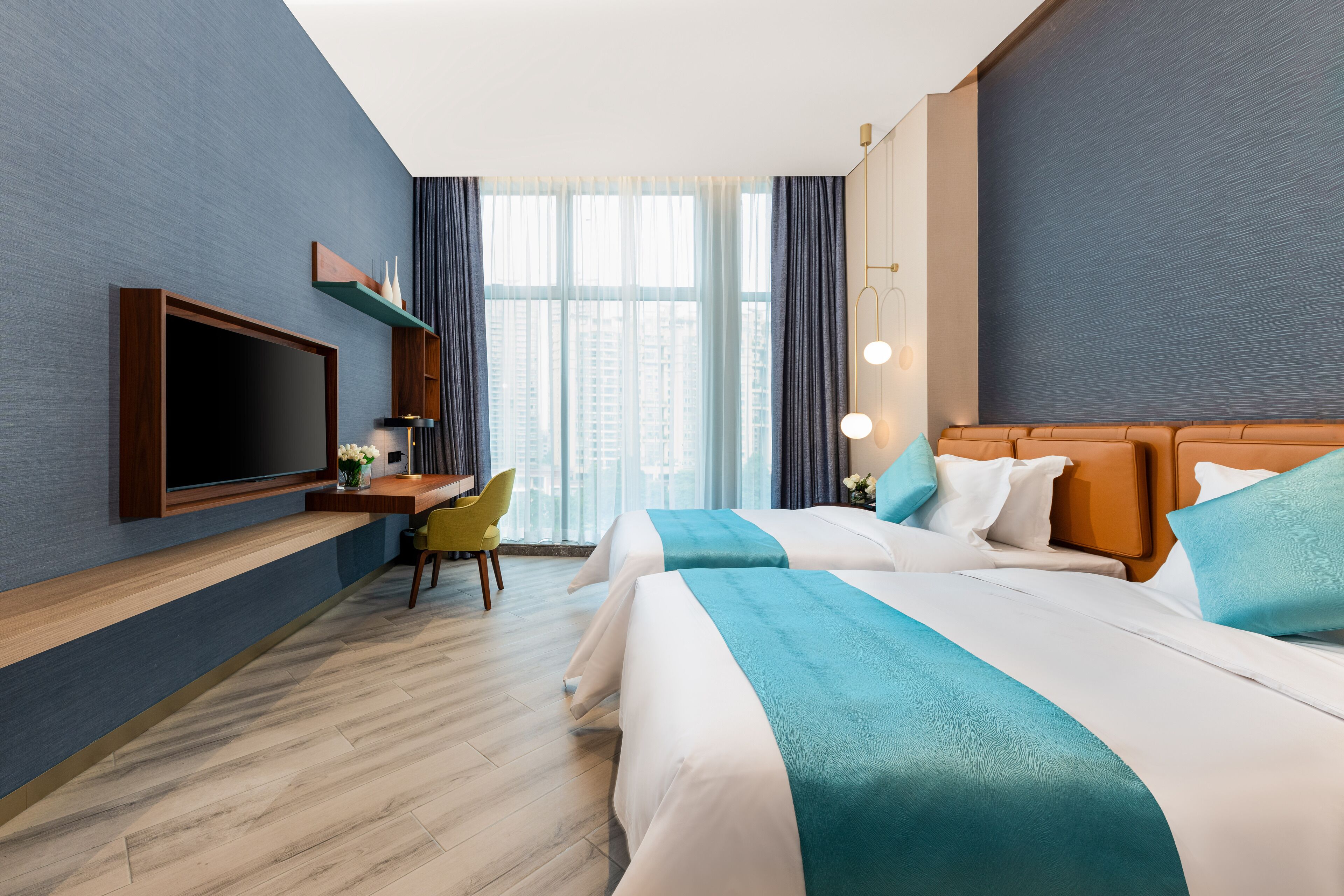 Habitación de hotel con dos camas, un escritorio, un televisor y un ventanal grande con cortinas.