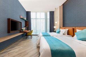 Habitación de hotel con dos camas, un escritorio, un televisor y un ventanal grande con cortinas.