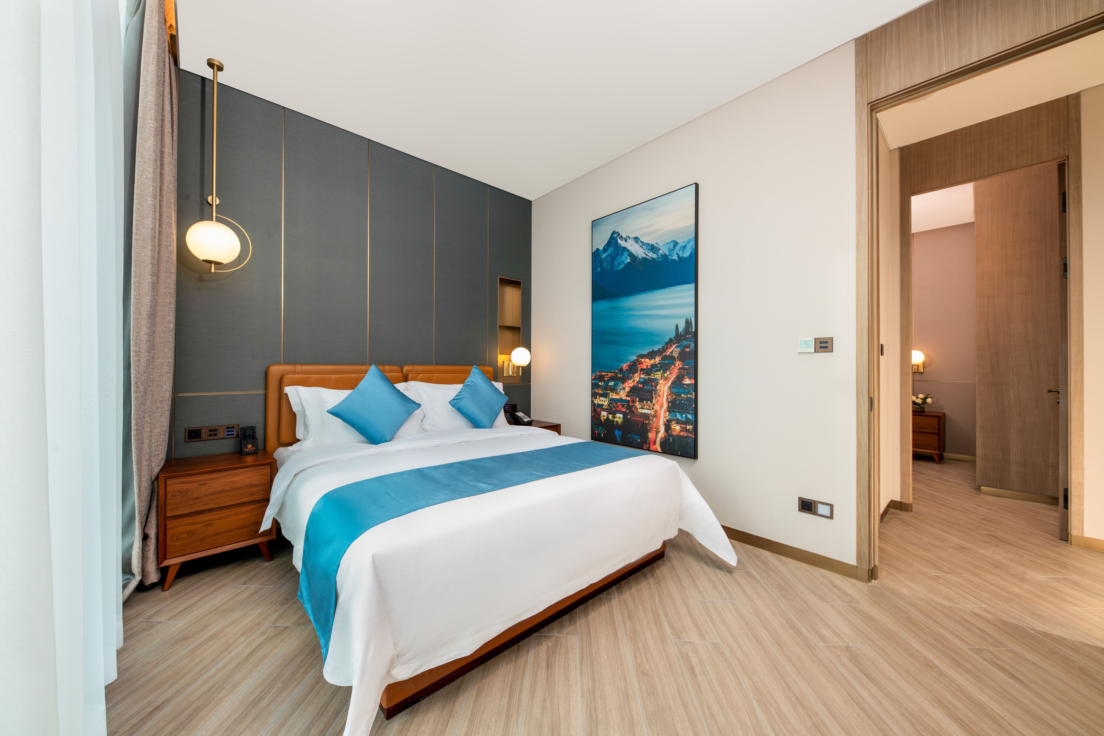 Una habitación de hotel moderna con una cama grande, cabecera de madera y un cuadro de paisaje urbano en la pared.