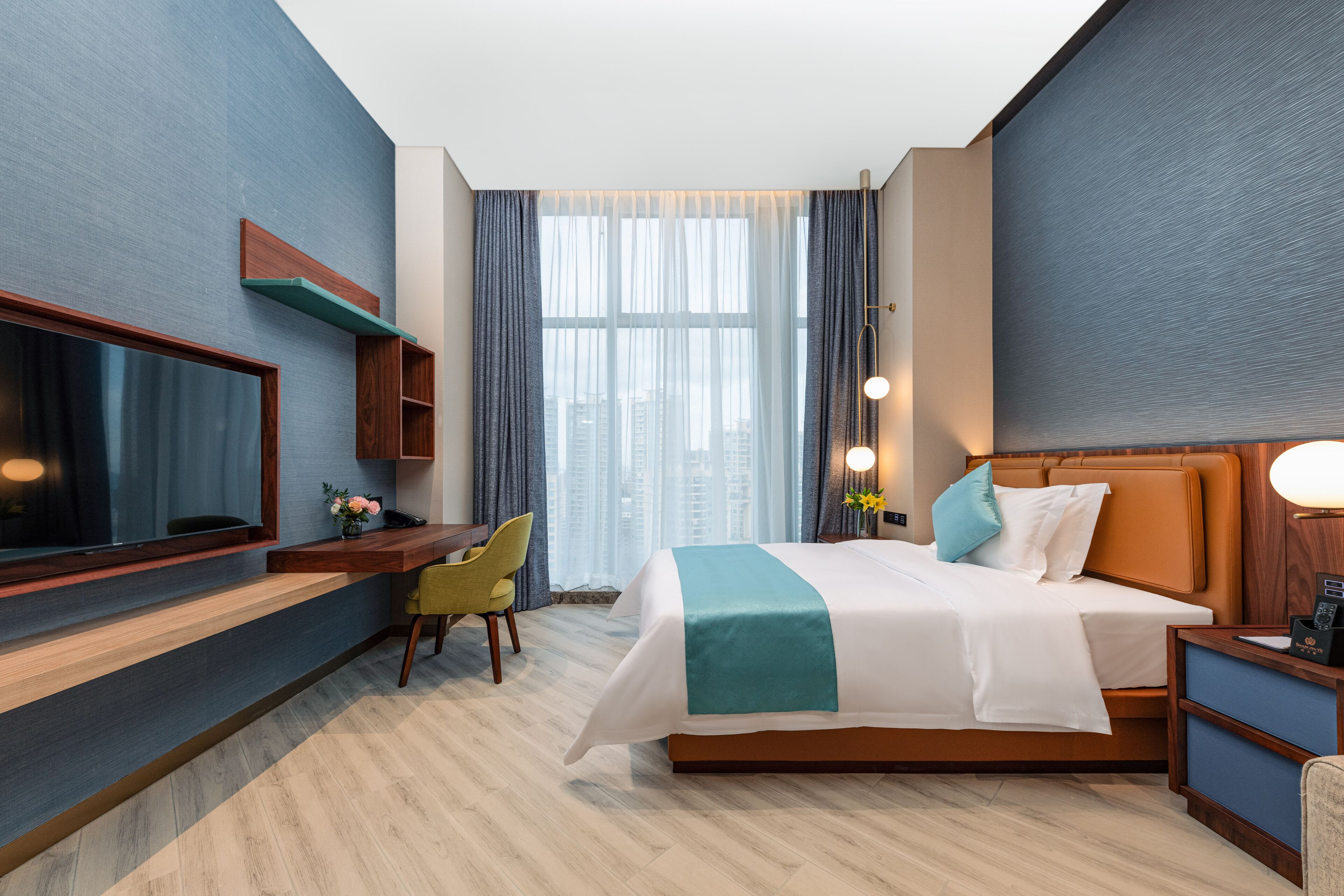 A modern hotel room with a large bed, a desk, a TV, and a view of the city.