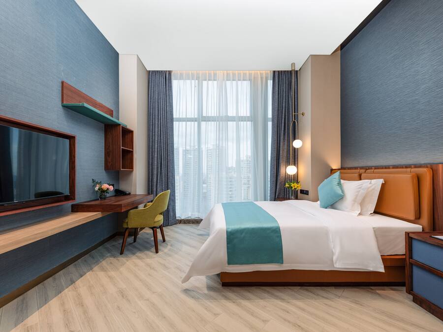 A modern hotel room with a large bed, a desk, a TV, and a view of the city.