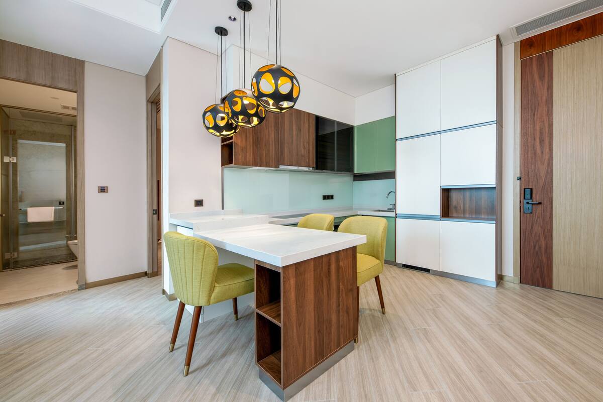 A modern kitchen with a central island, yellow chairs, and pendant lights.