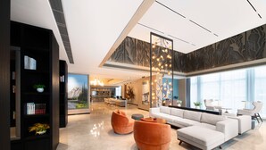Ein modernes Wohnzimmer mit einem weißen Sofa, orangefarbenen Sessel, einem Bücherregal und einem großen Fenster mit Blick auf einen Berg und Bäume.