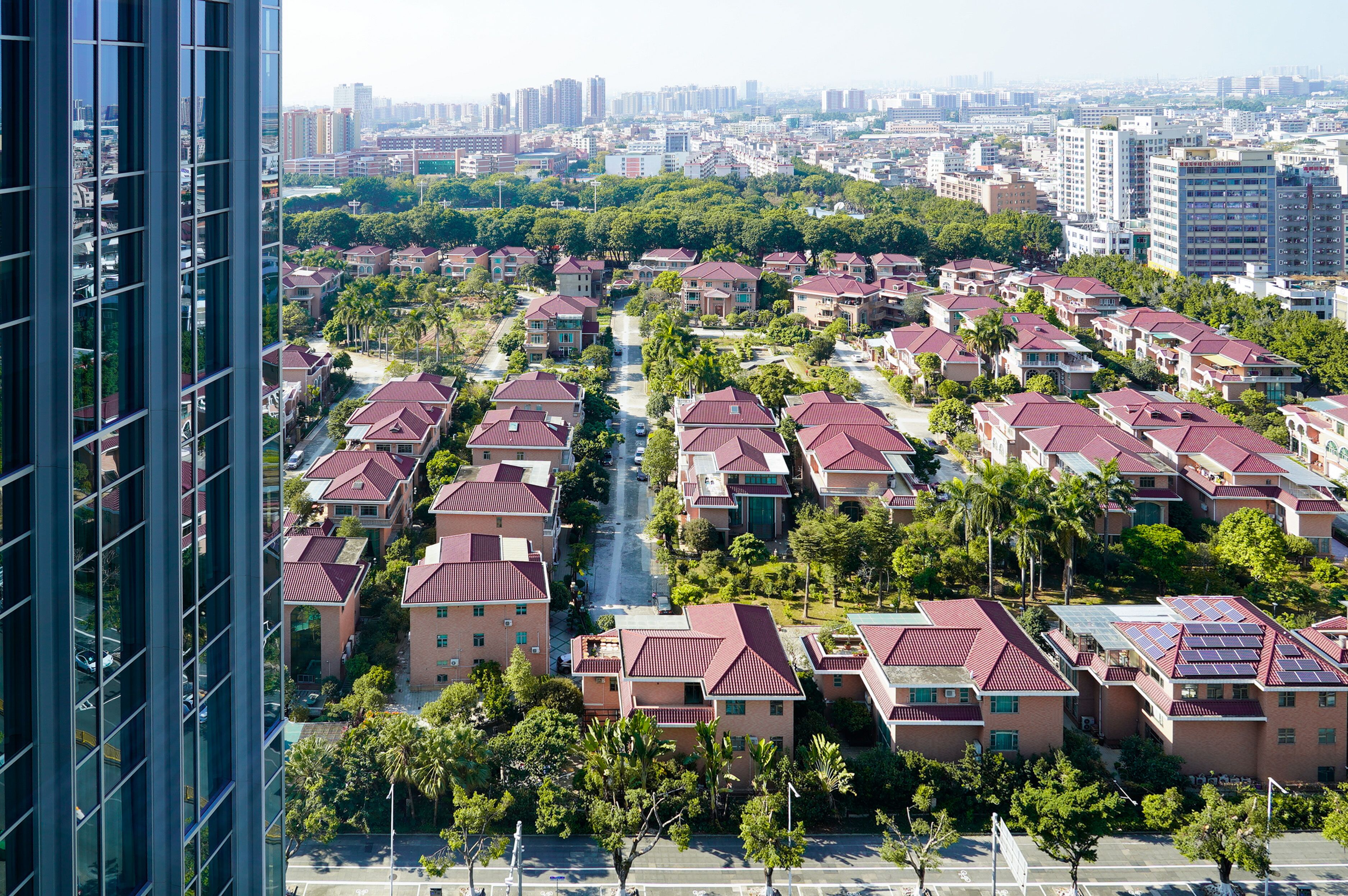 Un quartier résidentiel caractérisé par des maisons aux toits rouges de style uniforme, une rue principale et un grand immeuble en premier plan.