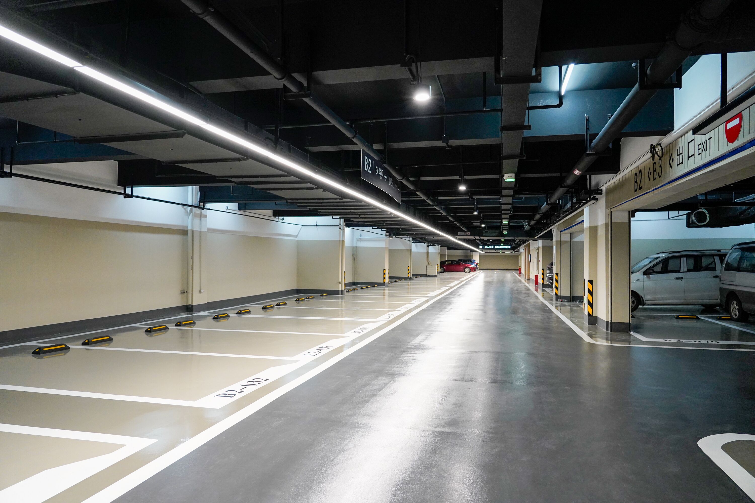 A parking garage with clear lane markings, overhead lighting, and exit signs.