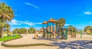 Explore the playground area surrounded by palm trees and a sandy space with climbing elements and slides.